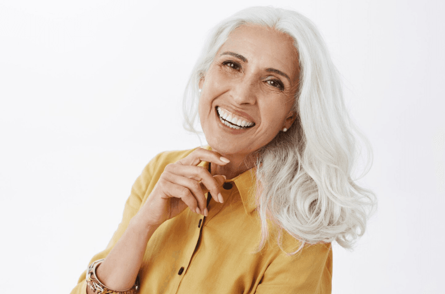 An elderly woman with flowing white hair gives a toothy grin.