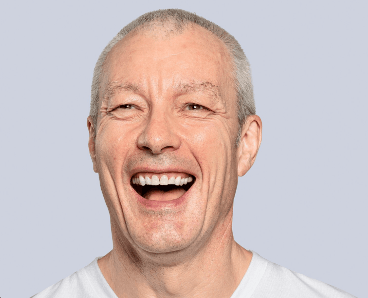 An elderly man smiles happily showing his teeth.