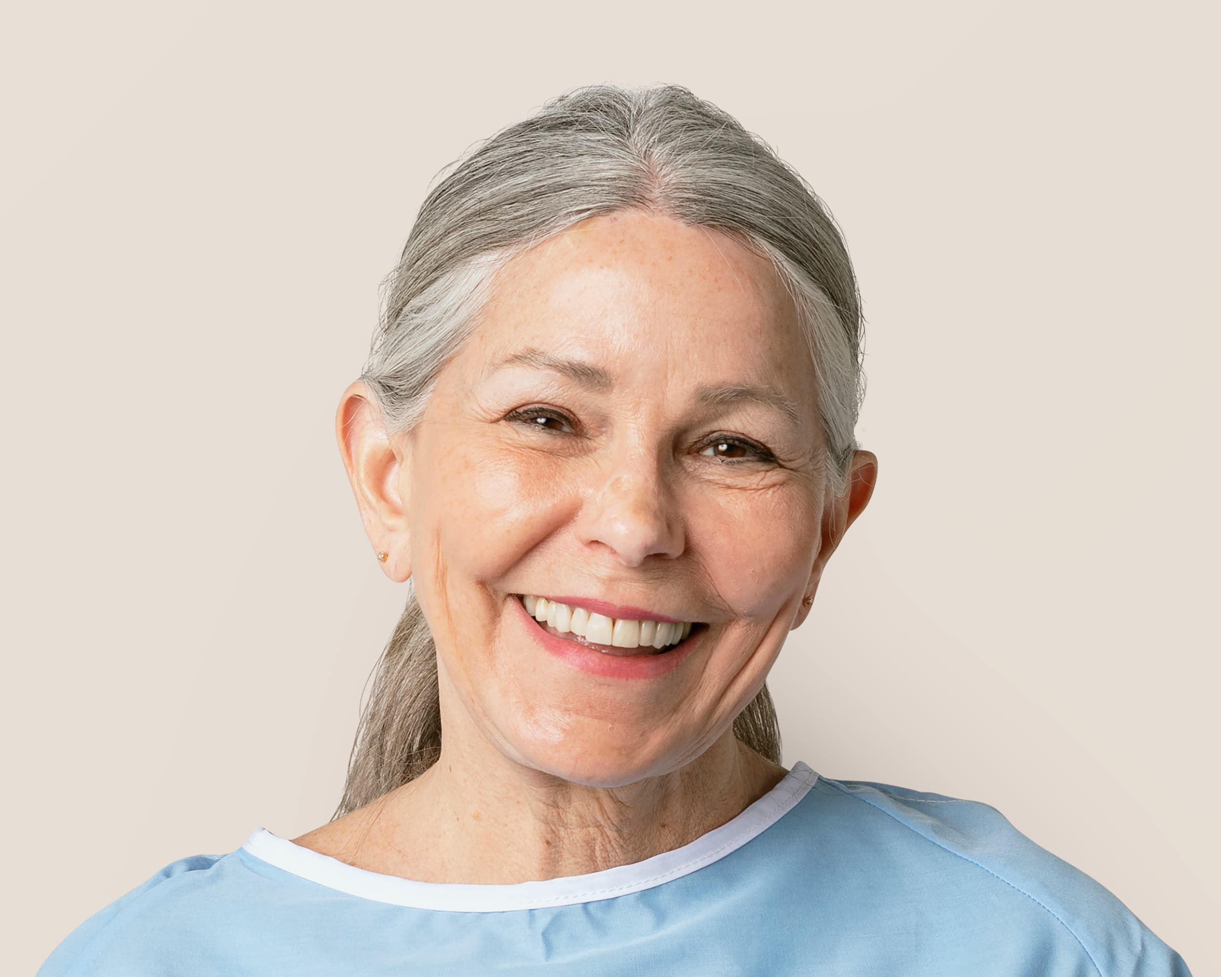 An elderly woman in a dental gown smiles brightly at the camera.