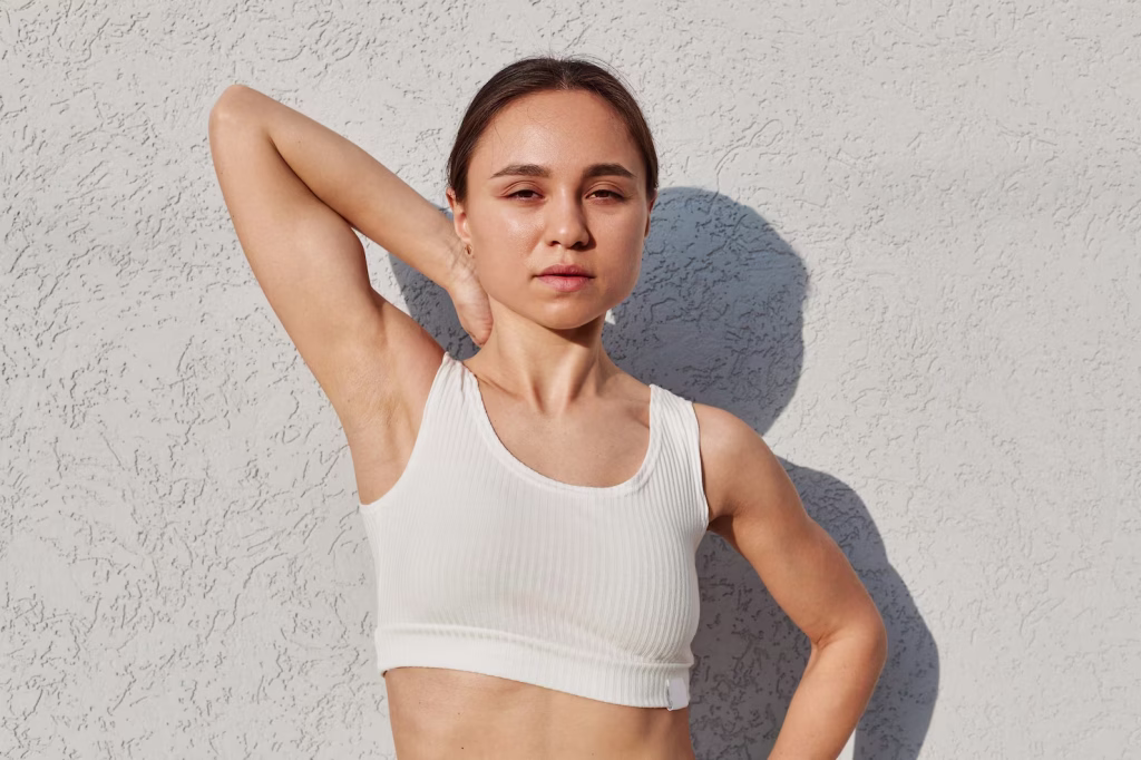 A young athletic girl posts with one of her hands raised exposing the armpit