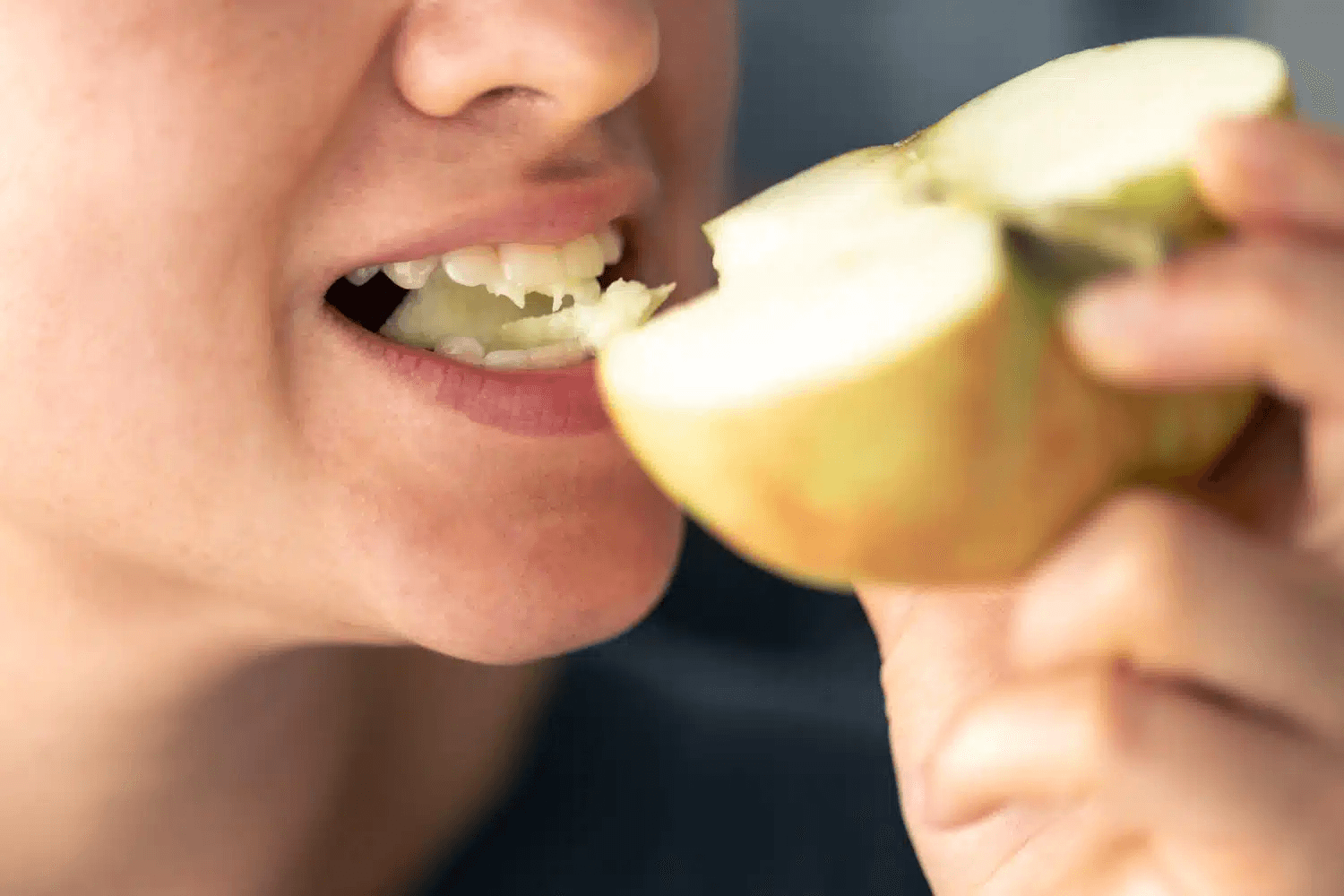 A person takes a bite out of a fresh apple cut in half.