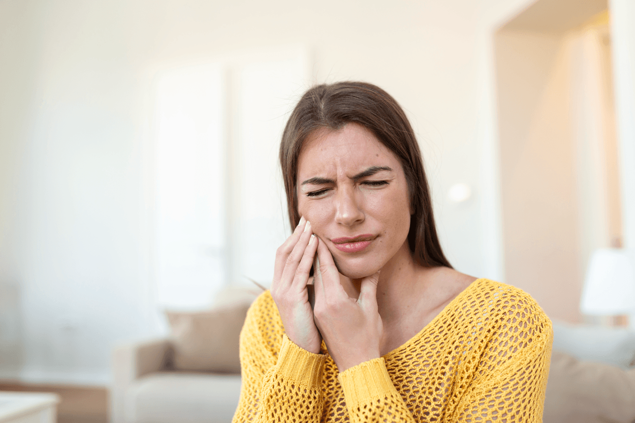 A woman touches her cheek visibly showing signs of terrible pain.