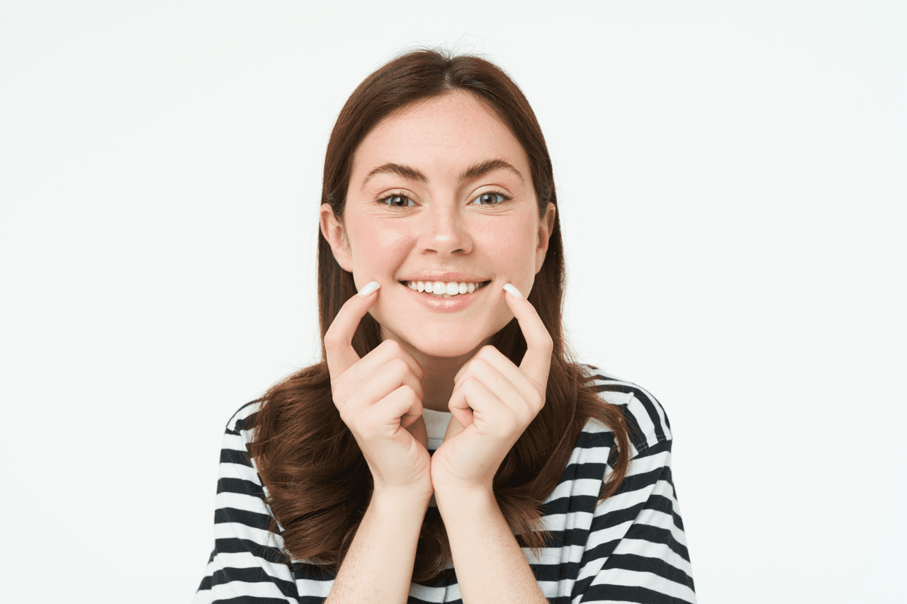 A woman smiles happily looking at the camera with her fingers touching the corners of her mouth