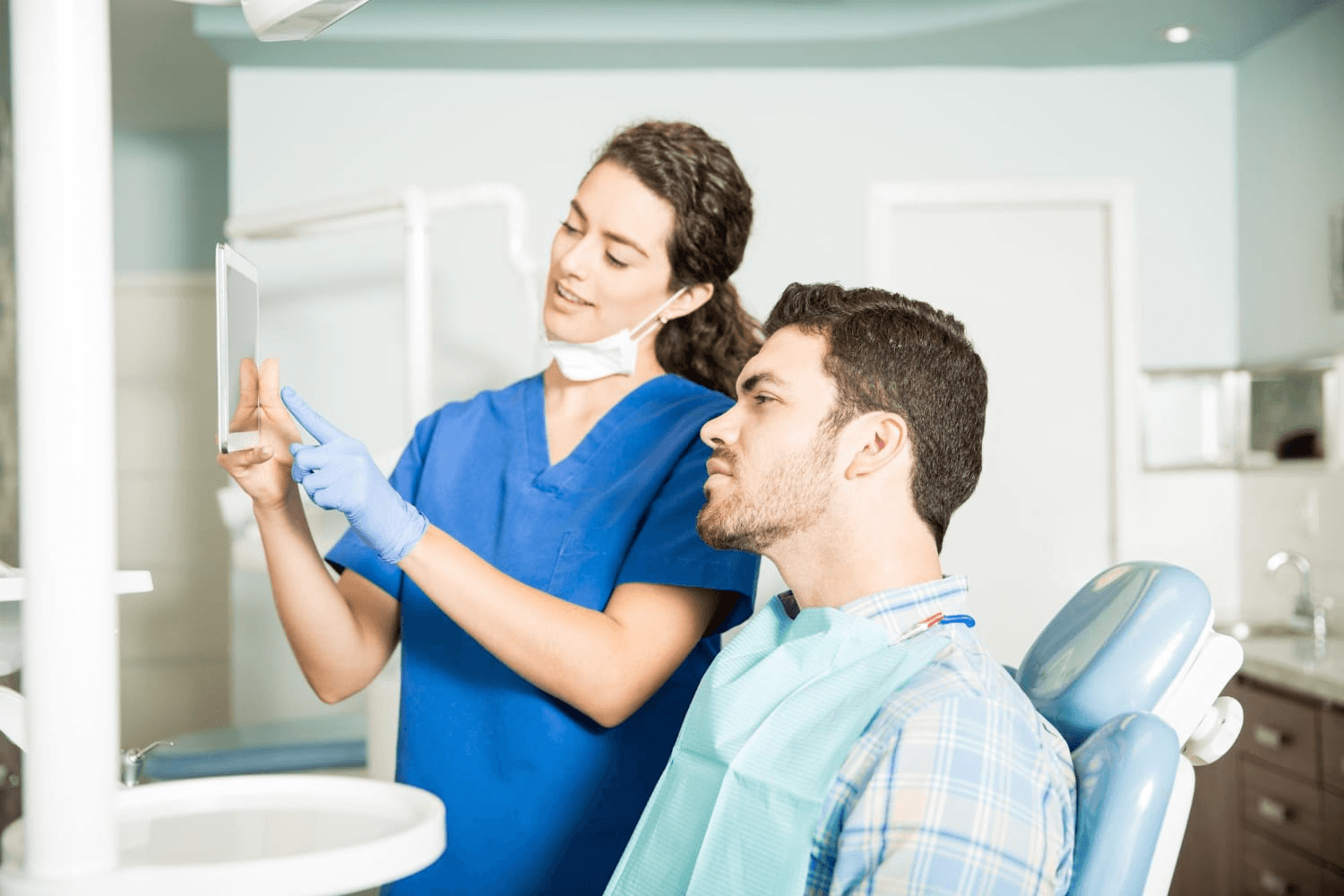 A dentists holds up a scan and explains a dental procedure to a patient at a clinic.