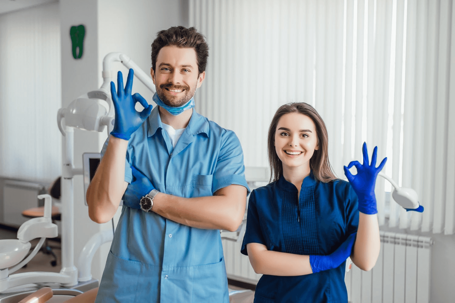 A male and female stand inside a clinic smiling and doing the "ok" hand sign