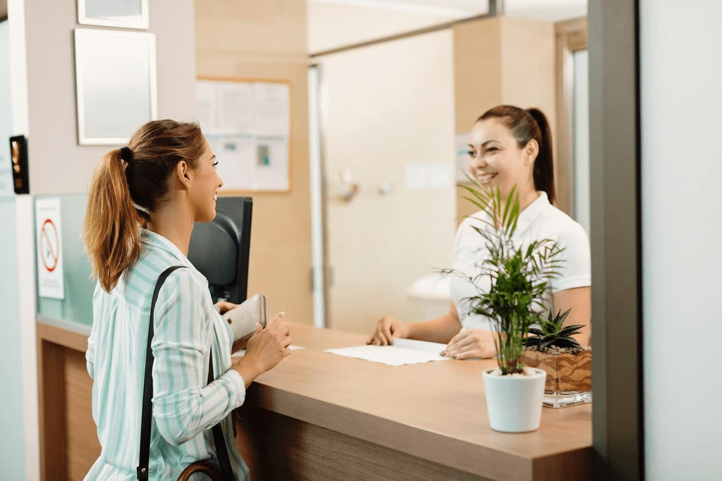 A patient speaks with a smiling receptionist at a dental clinic.